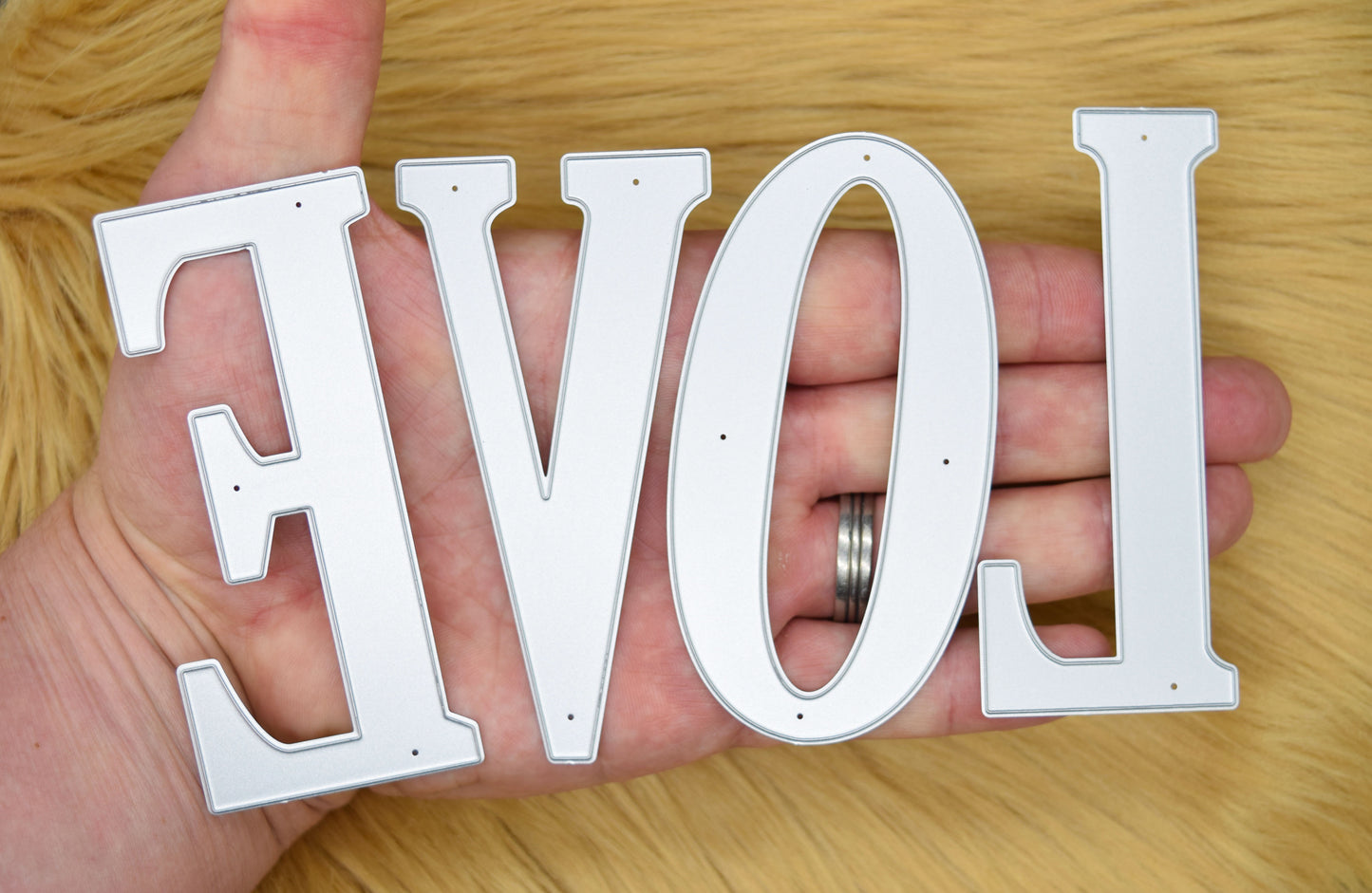 Large uppercase letter metal cutting dies held across a hand to demonstrate their substantial 10 cm size.