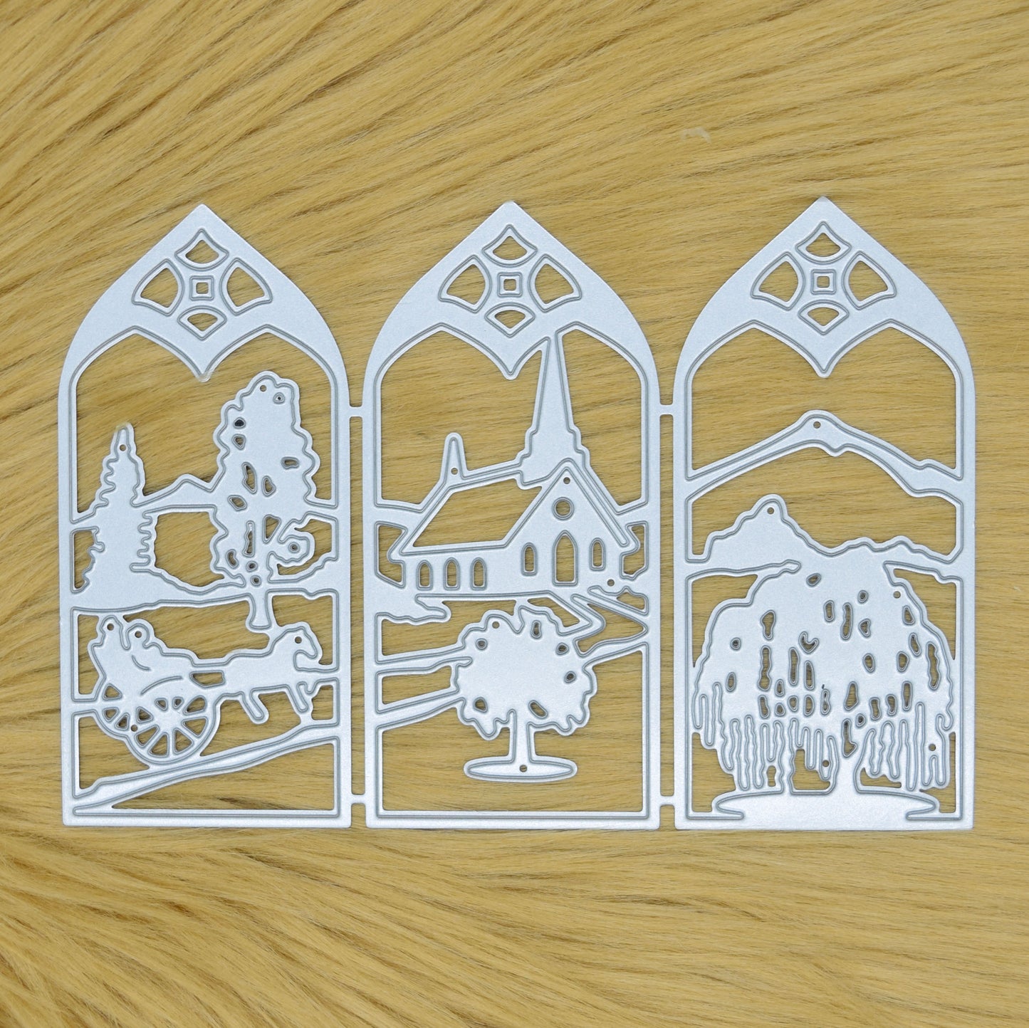 Countryside window scene metal cutting die displayed on a light faux fur background, featuring three connected decorative landscape panels.