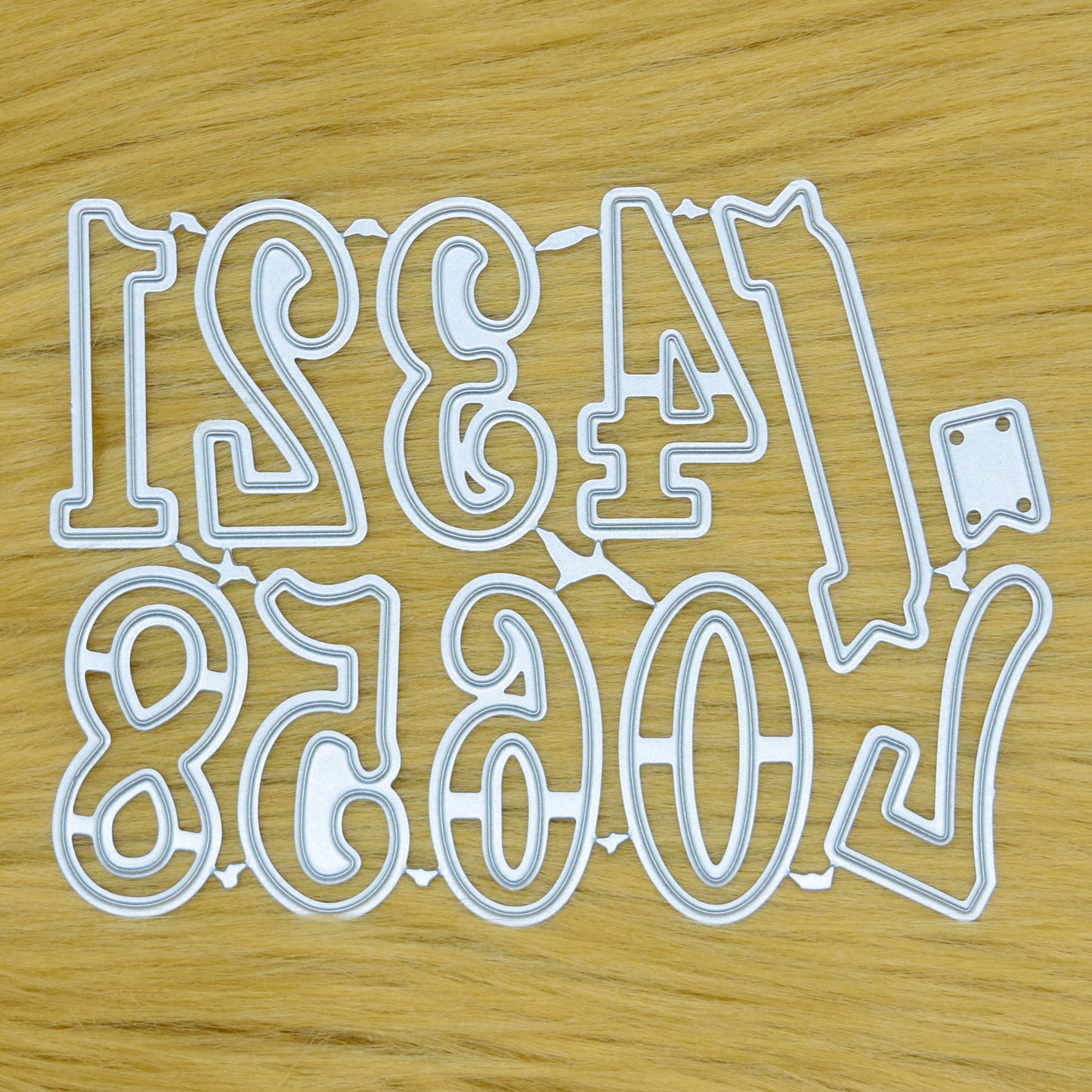 Decorative number metal cutting dies from zero to nine with a small banner die displayed on a tan faux fur background.