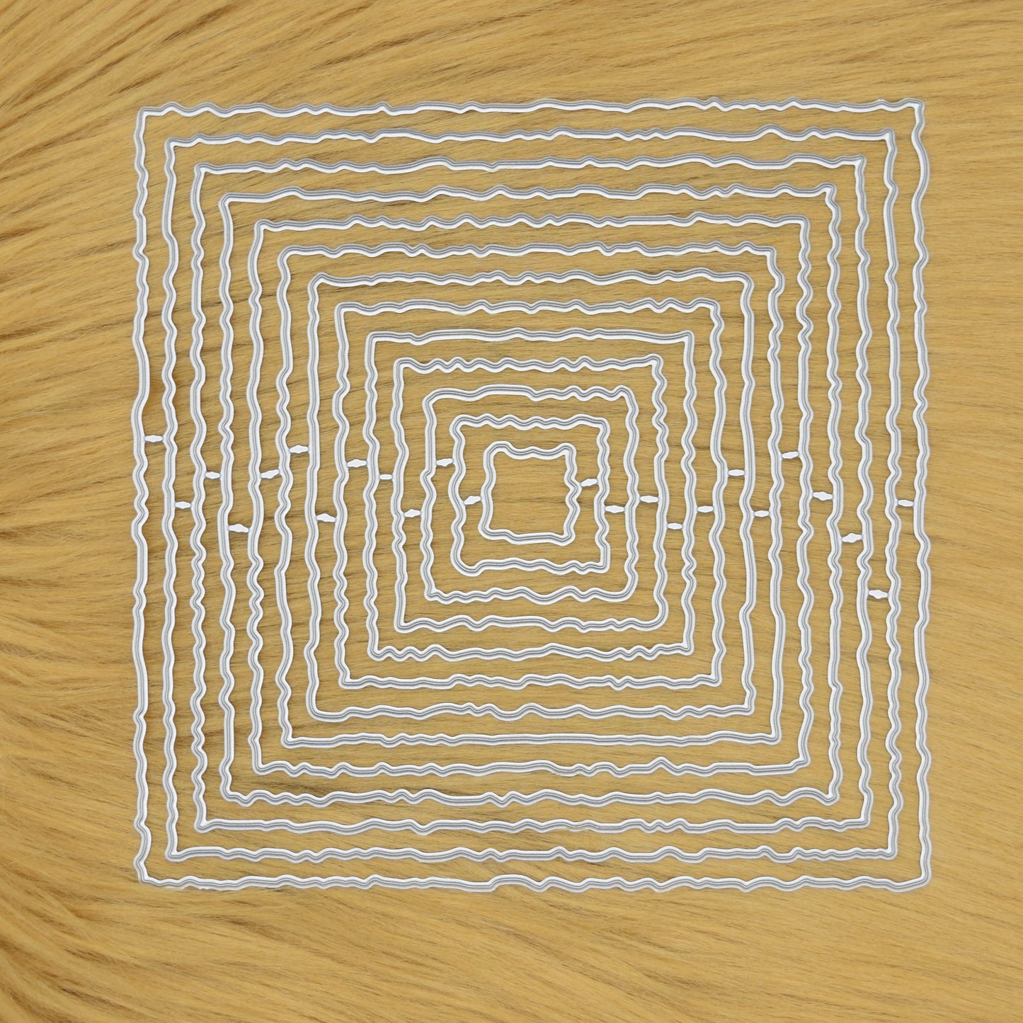 Set of thirteen torn edge square nesting metal cutting dies arranged on a faux fur background