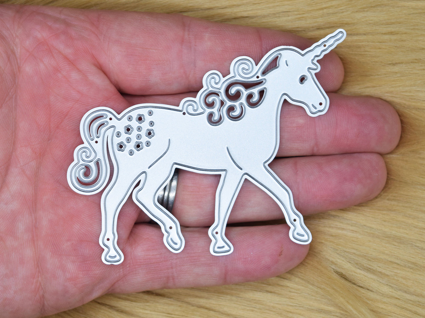 Unicorn metal cutting die shown in hand for size reference
