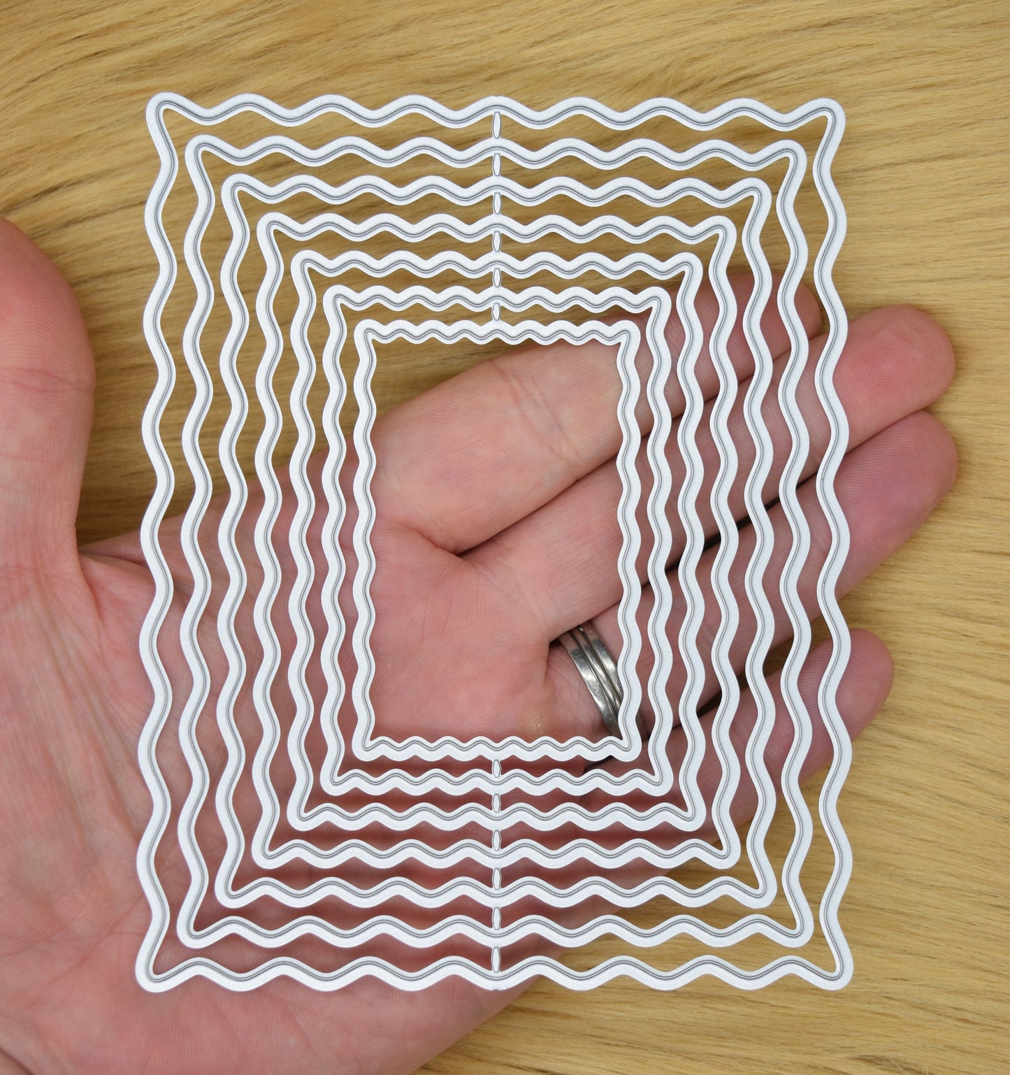 Wavy rectangle nesting dies shown in hand for size reference