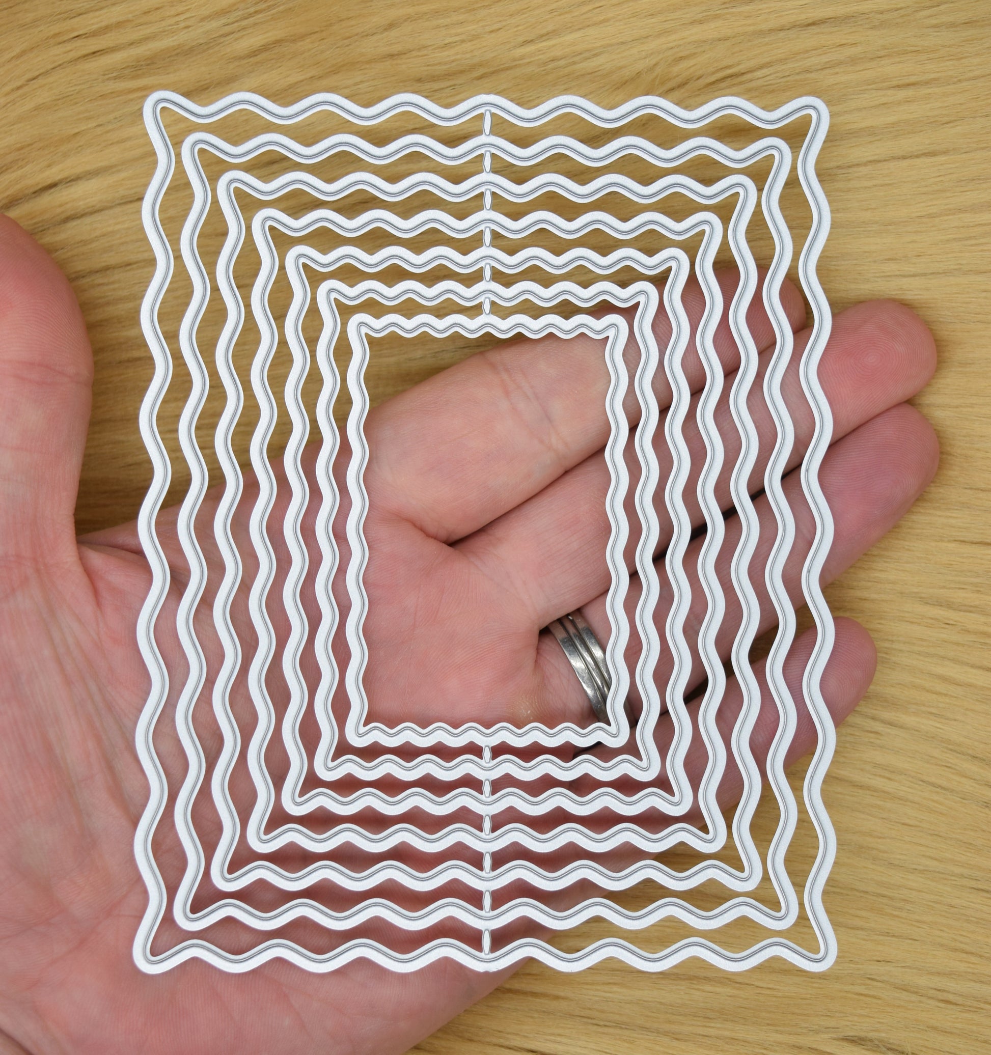Wavy rectangle nesting dies shown in hand for size reference