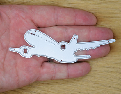 Jet airplane metal cutting die shown in hand for size reference featuring passenger aircraft silhouette design for card making