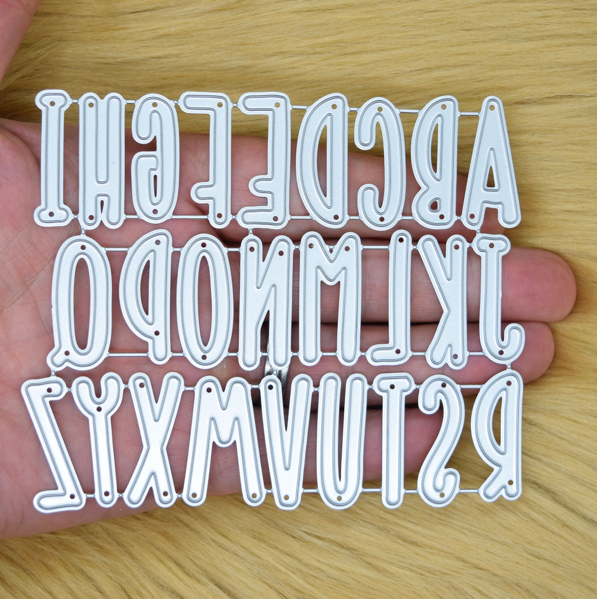 Uppercase alphabet metal cutting dies shown in hand for scale reference