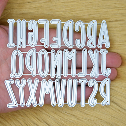 Uppercase alphabet metal cutting dies shown in hand for scale reference