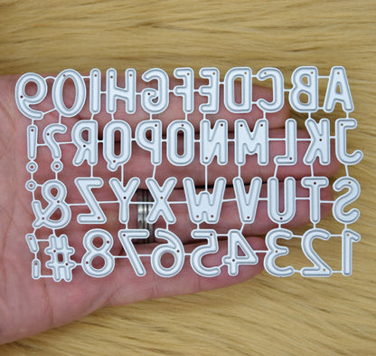 Alphabet and number metal cutting dies shown in hand for scale
