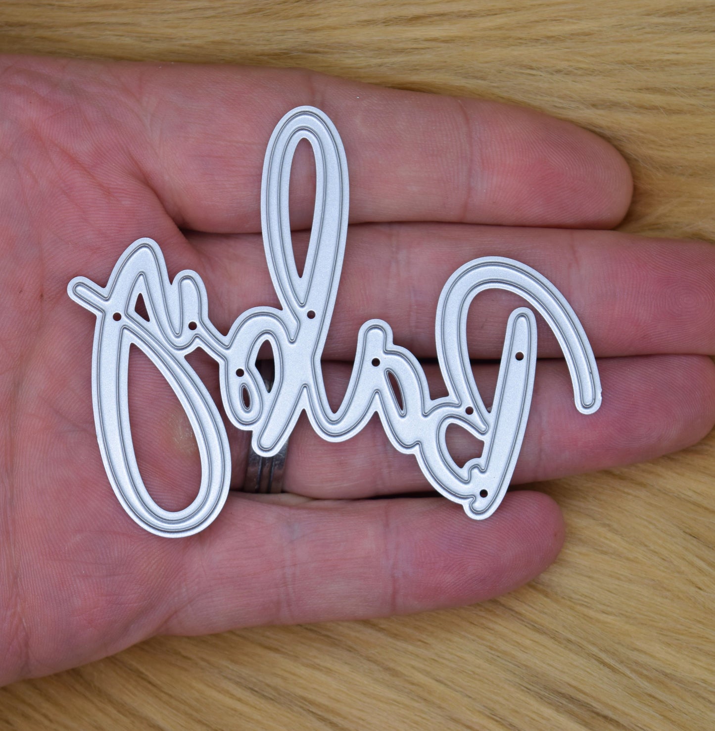 Baby script sentiment metal cutting die shown in hand for size reference