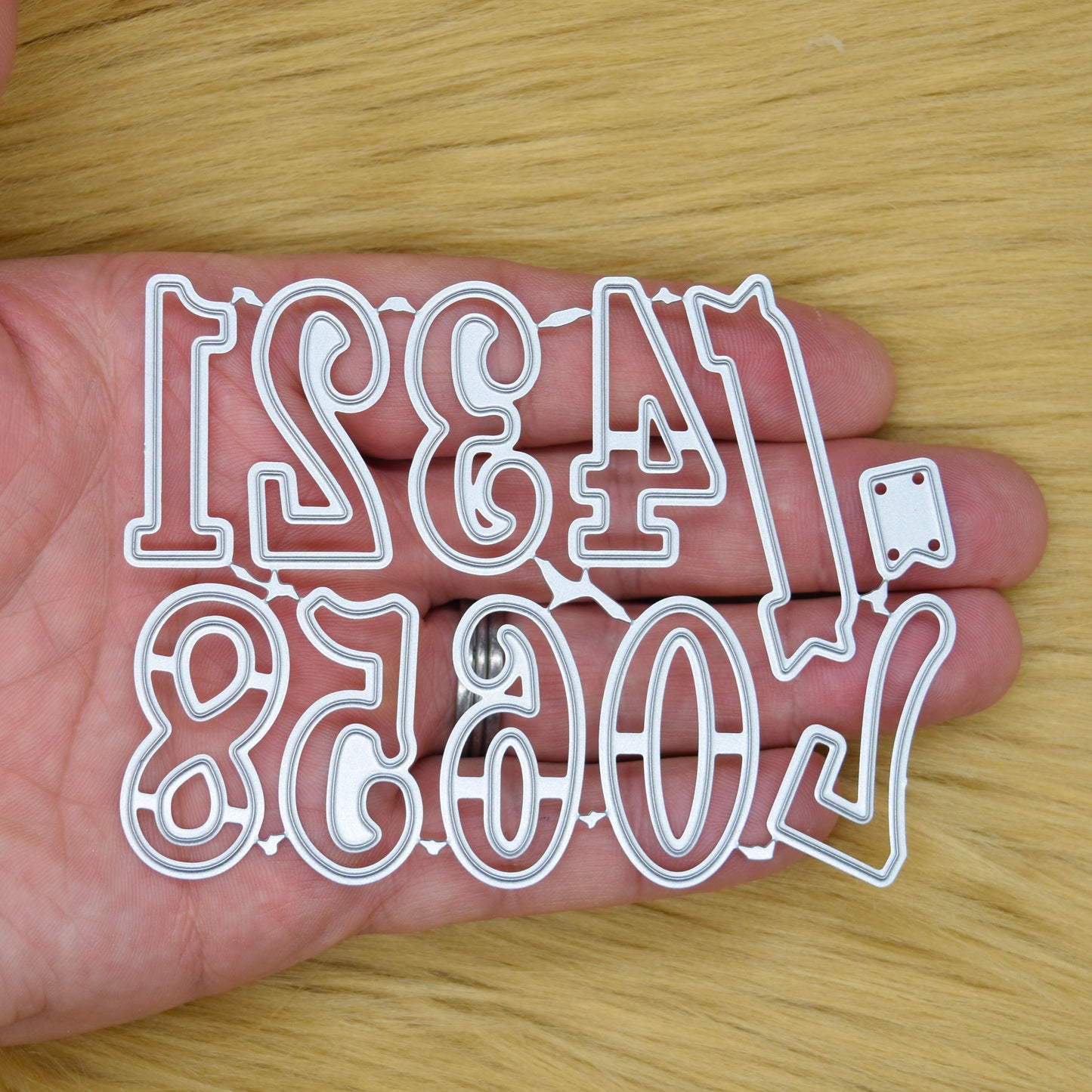 Decorative number and banner metal cutting dies held in a hand to show their size and individual numeral designs.
