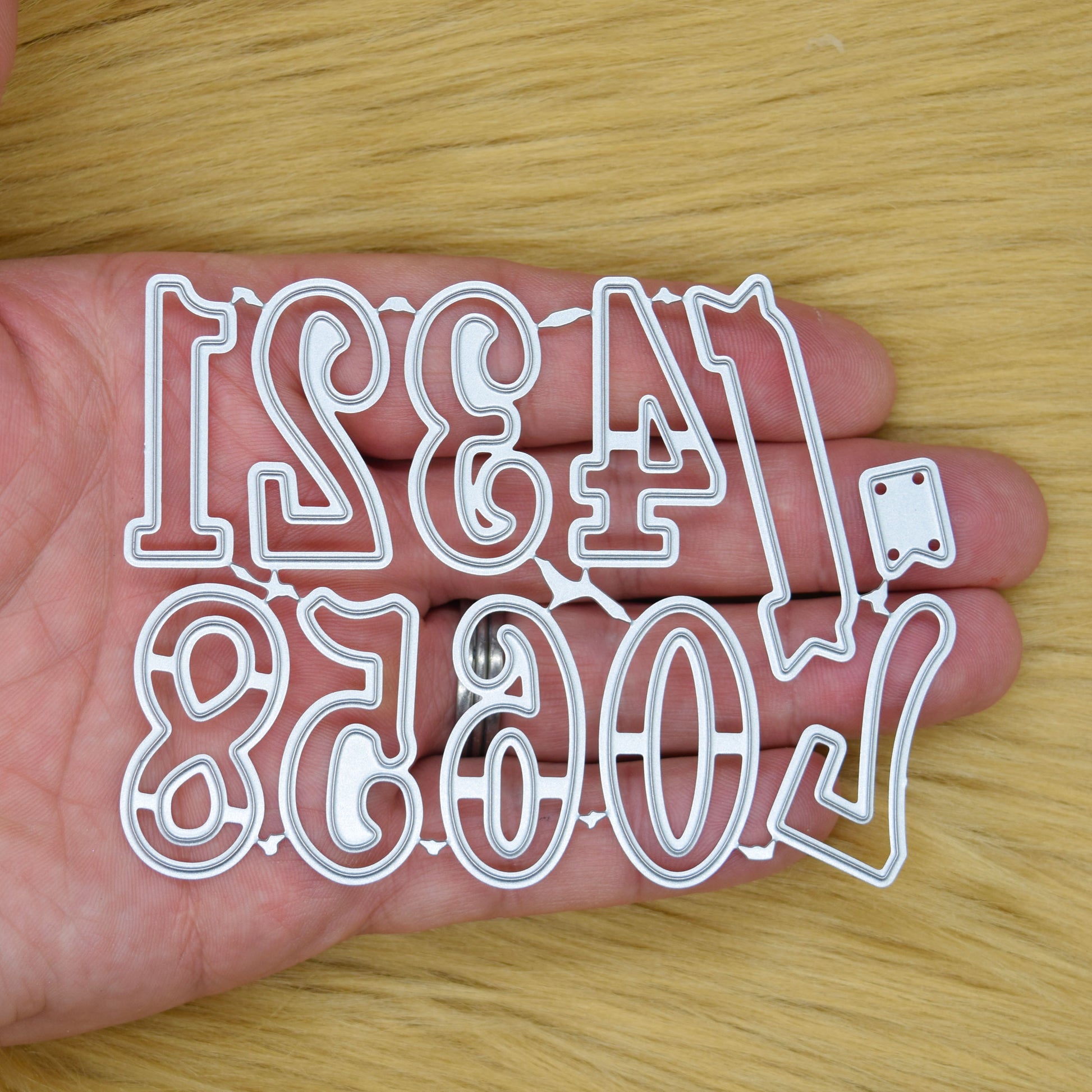 Decorative number and banner metal cutting dies held in a hand to show their size and individual numeral designs.
