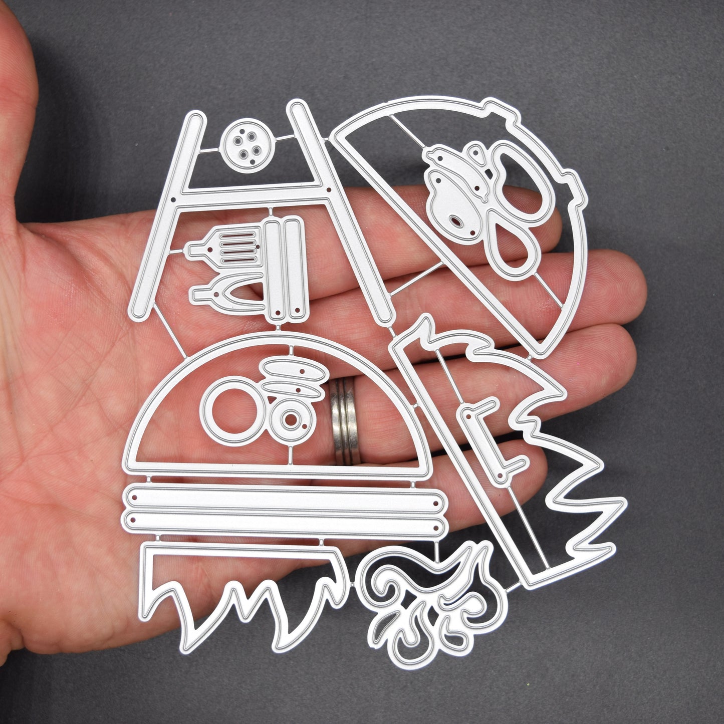 Large BBQ barbecue grill and accessories metal cutting die set shown in hand on dark background for size reference and papercraft use