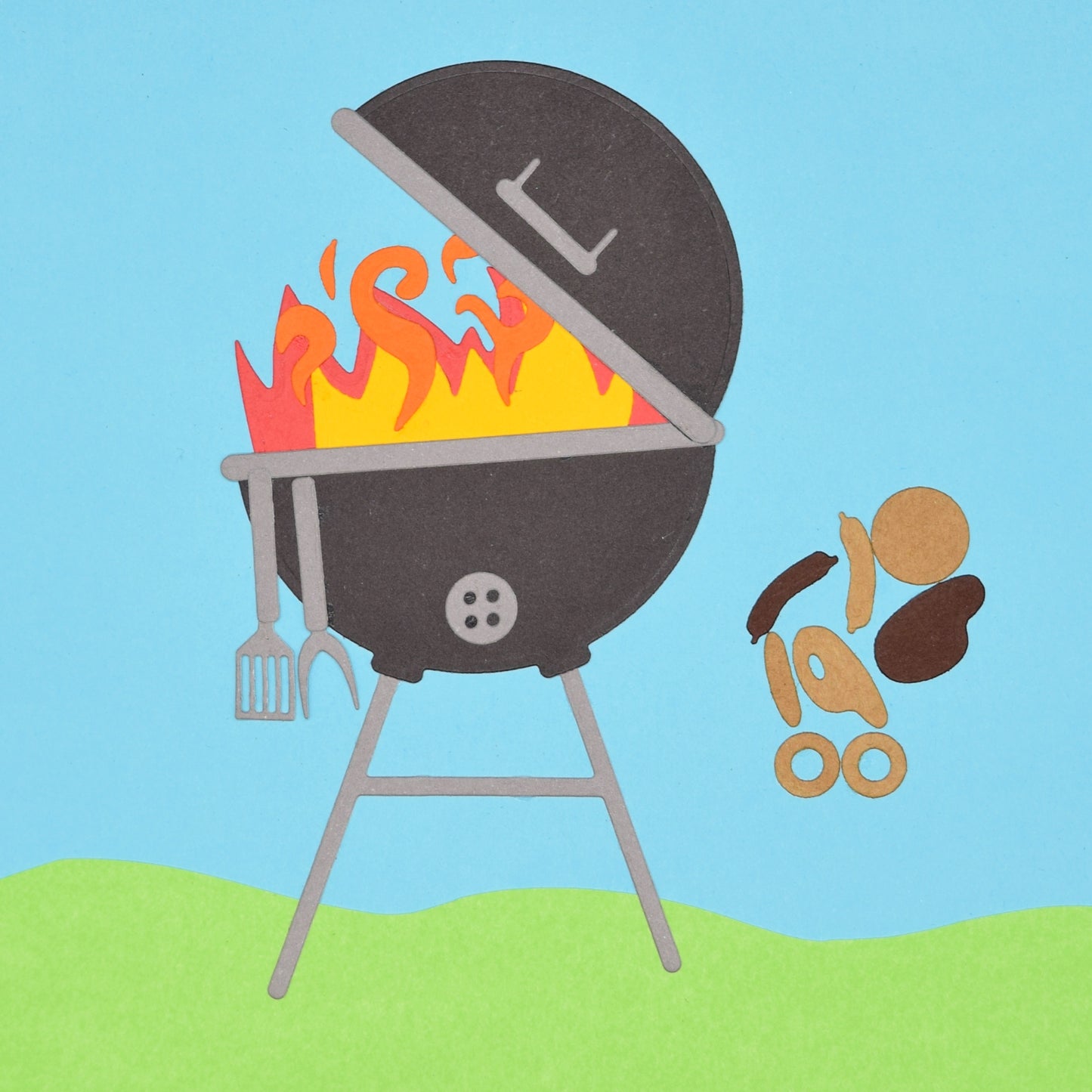 Finished BBQ barbecue grill paper craft made using metal cutting dies with flames cooking utensils and food pieces on blue background