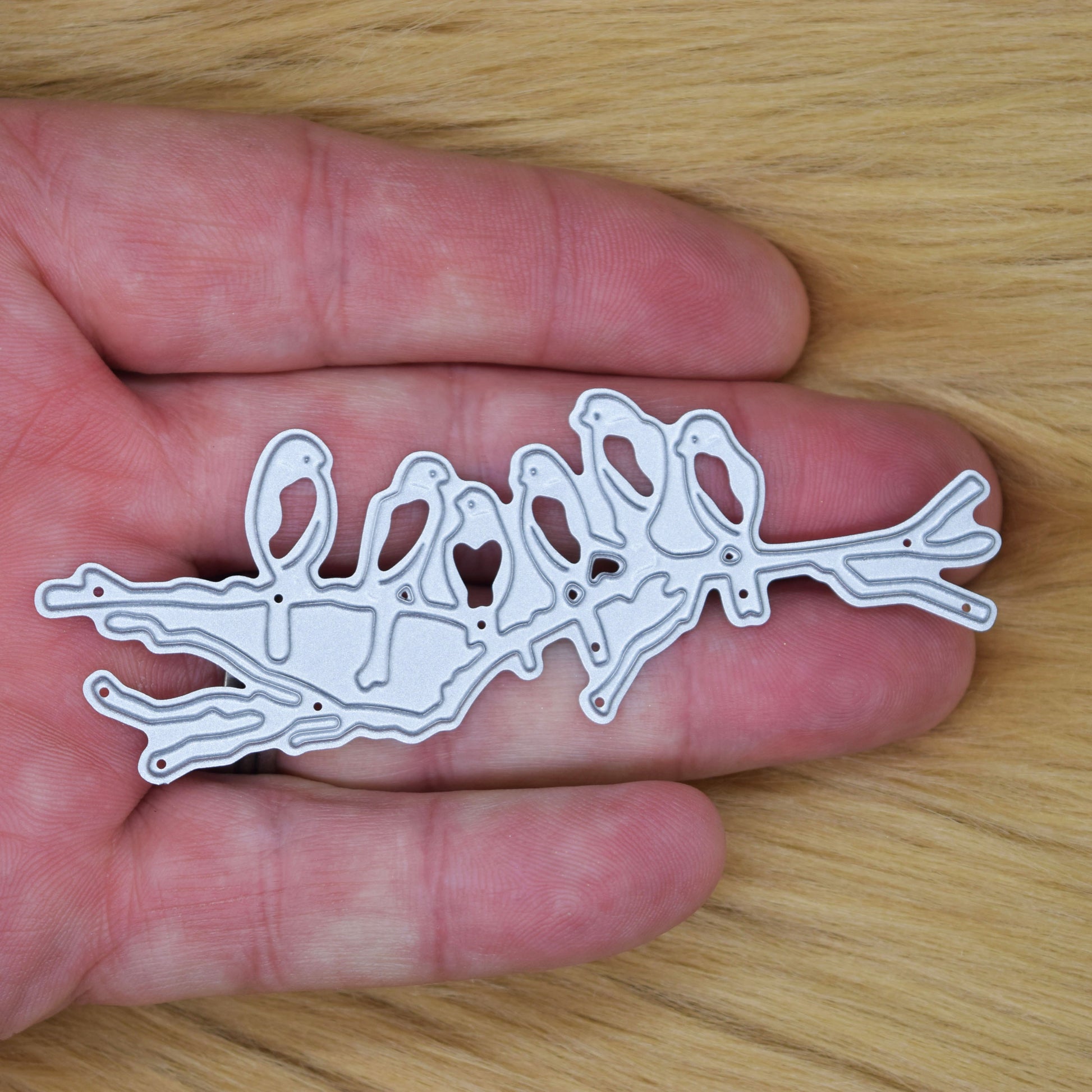 Birds on branch metal cutting die shown in hand for size reference
