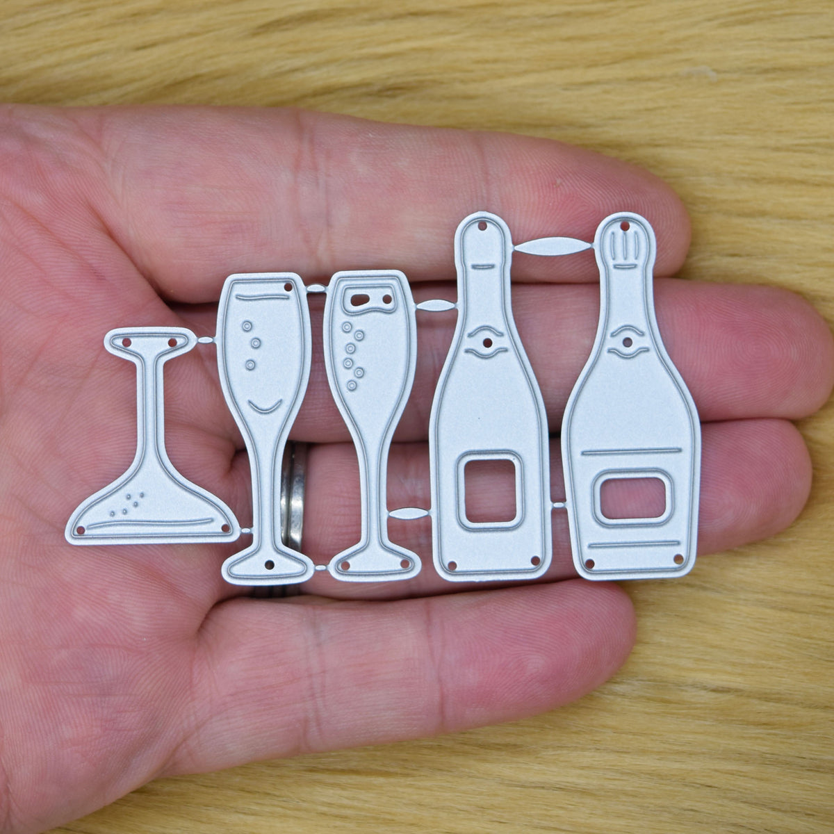 Champagne bottle and glass metal cutting die set held in a hand to show its size for wedding and anniversary card making.