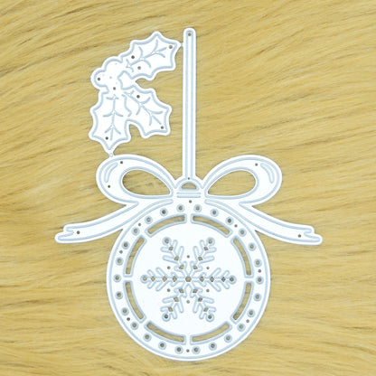 Christmas bauble and holly metal cutting die displayed on a tan faux fur background, showing the detailed snowflake and bow design.