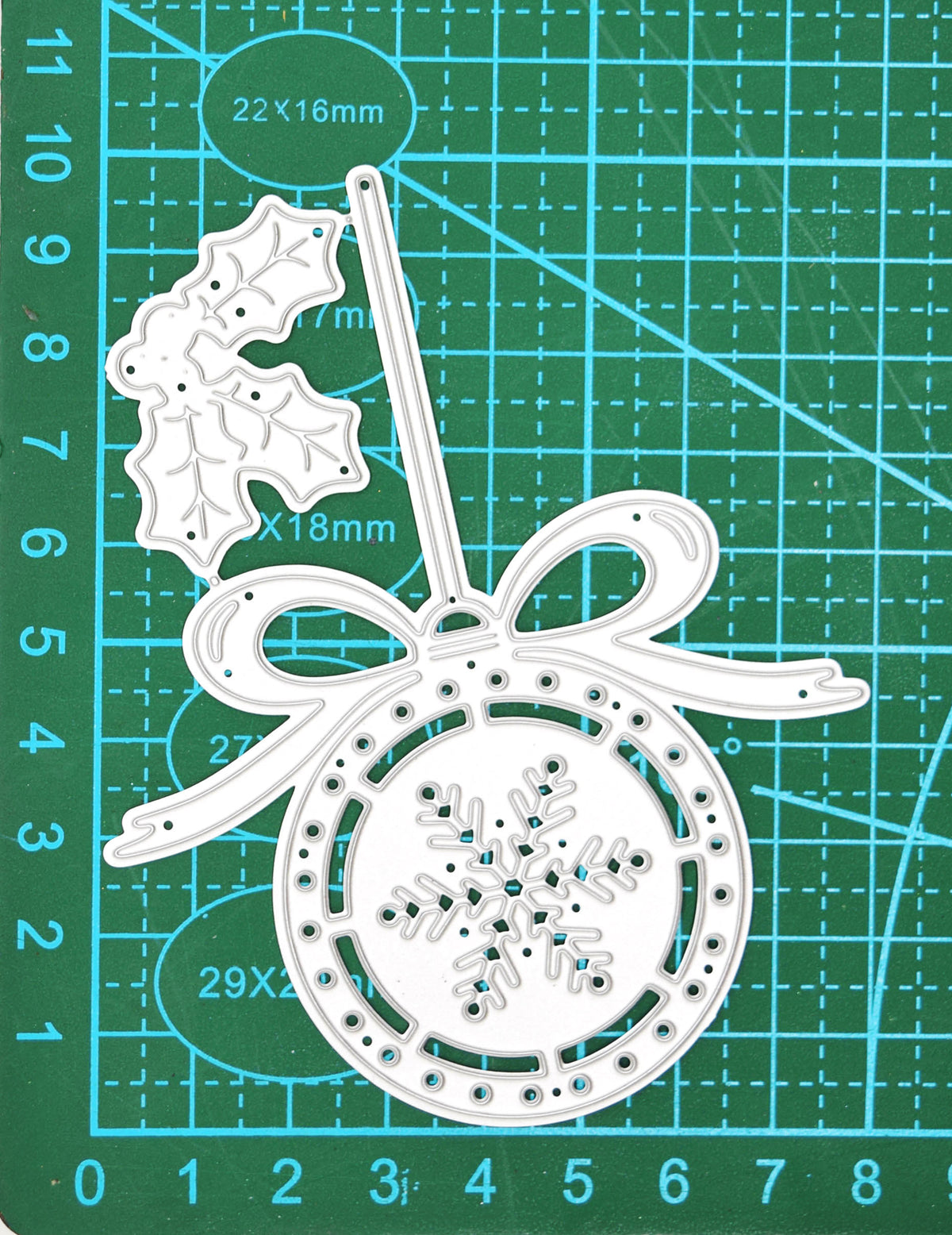 Christmas bauble and holly metal cutting die shown on a centimetre cutting mat for size reference.