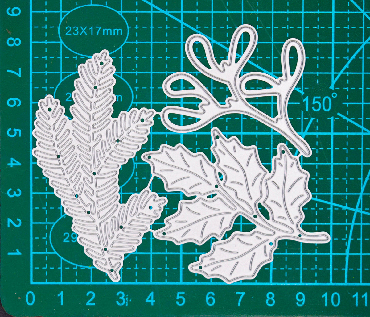 Christmas holly, pine and mistletoe metal cutting dies displayed on a cutting mat to show their approximate size.