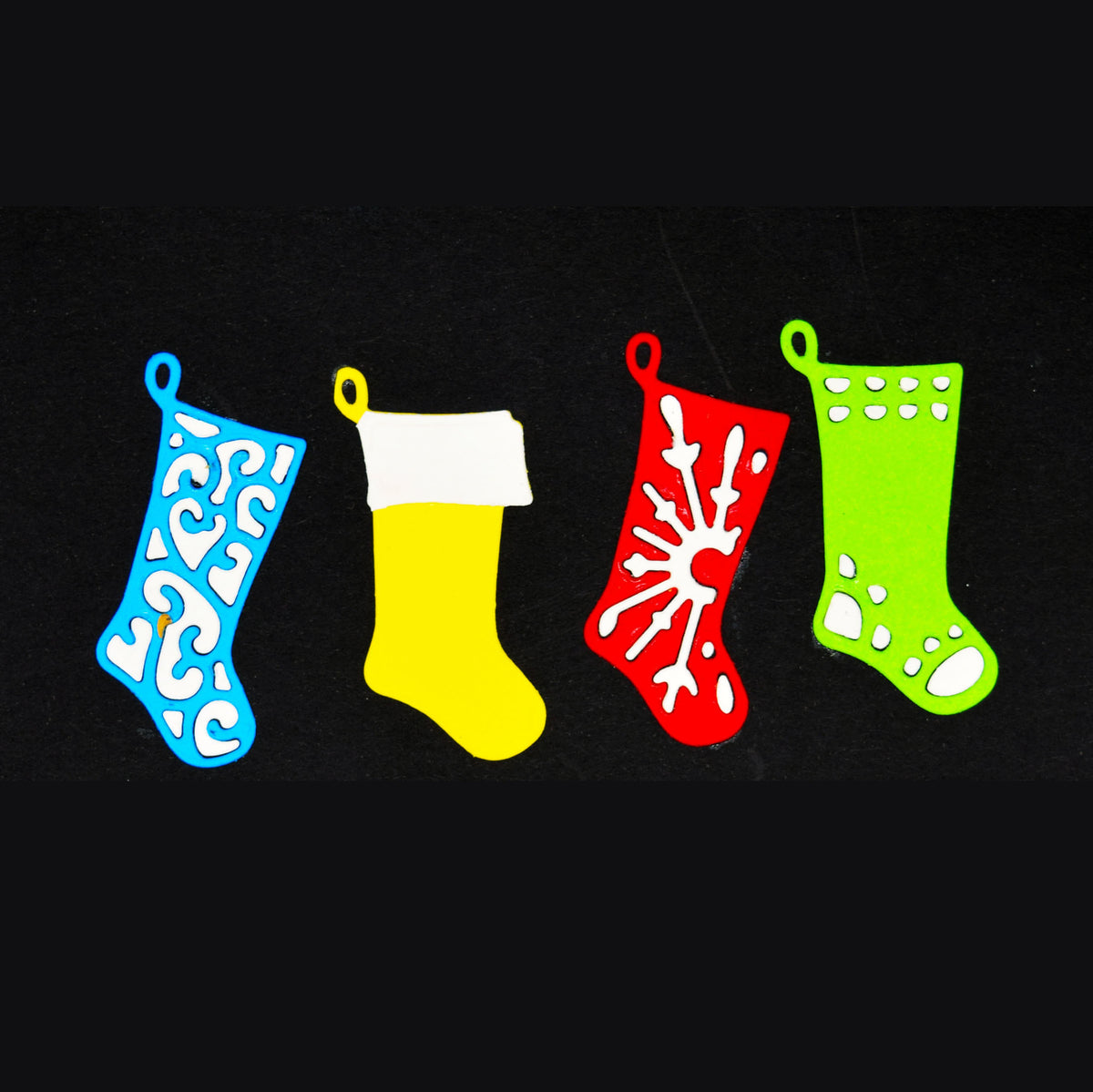 Blue, yellow, red and green Christmas stocking paper cuts with contrasting white details on a black background.