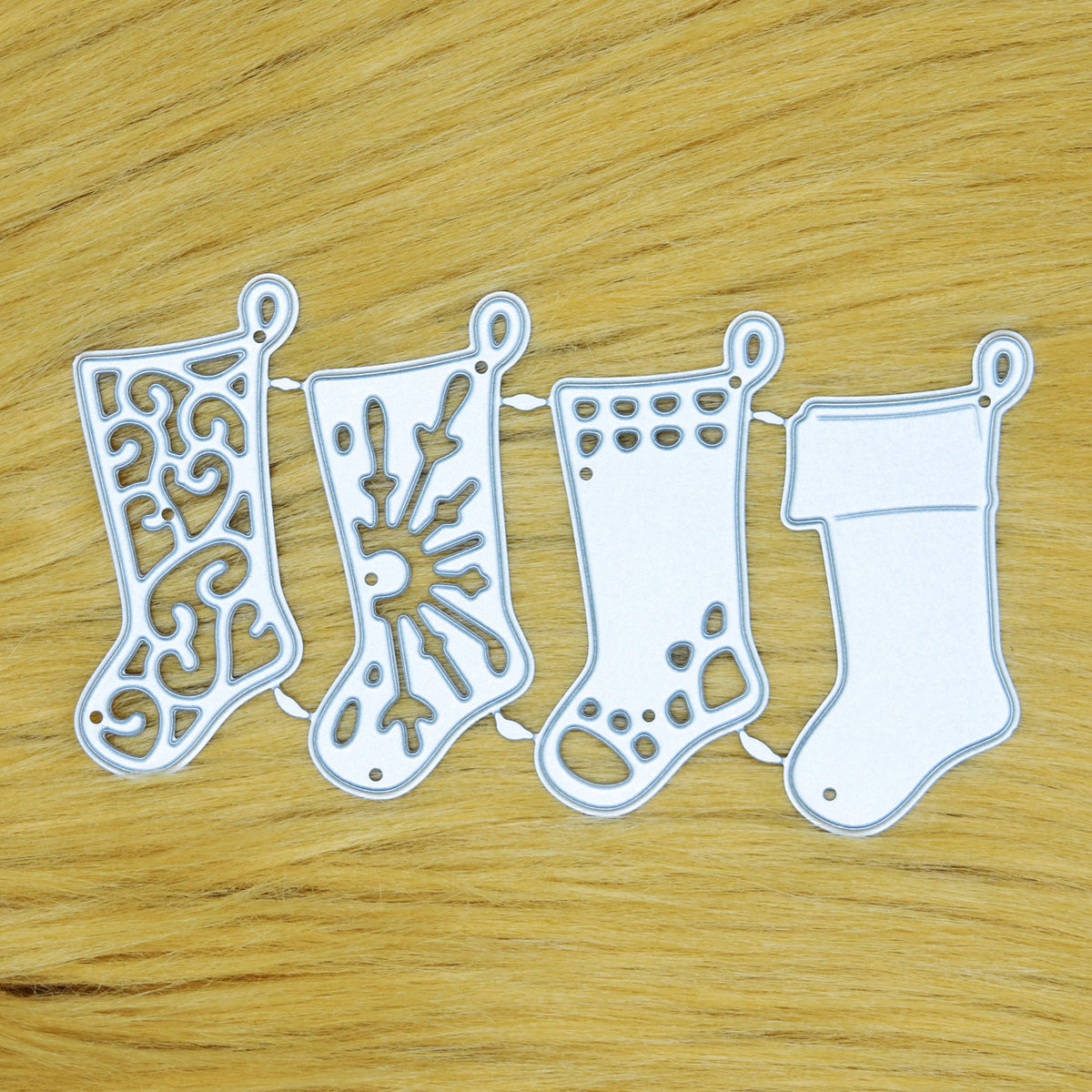 Four joined Christmas stocking metal cutting dies with different decorative designs on a tan faux fur background.