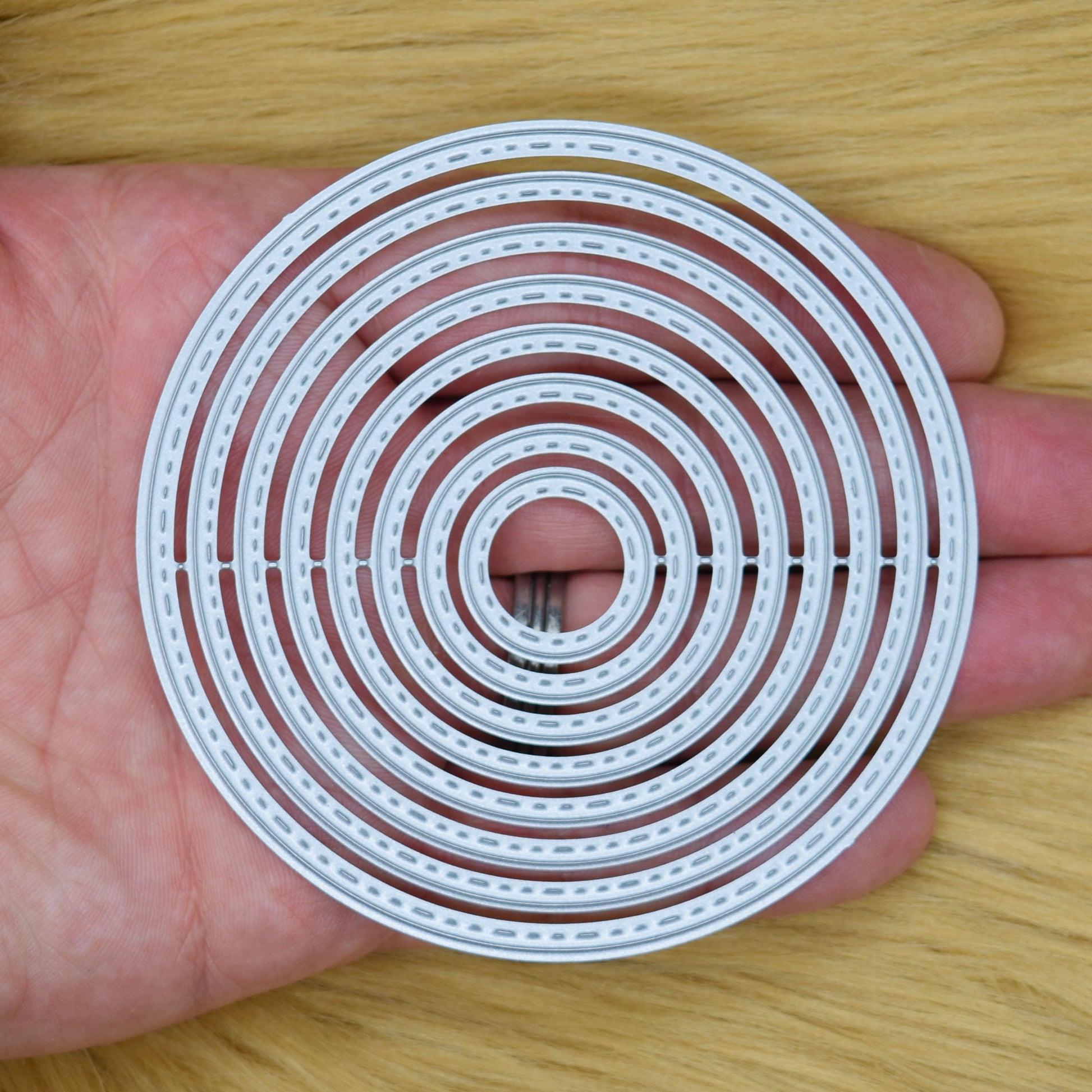 Eight stitched circle nesting metal cutting dies held in a hand to show the overall size and graduated design.
