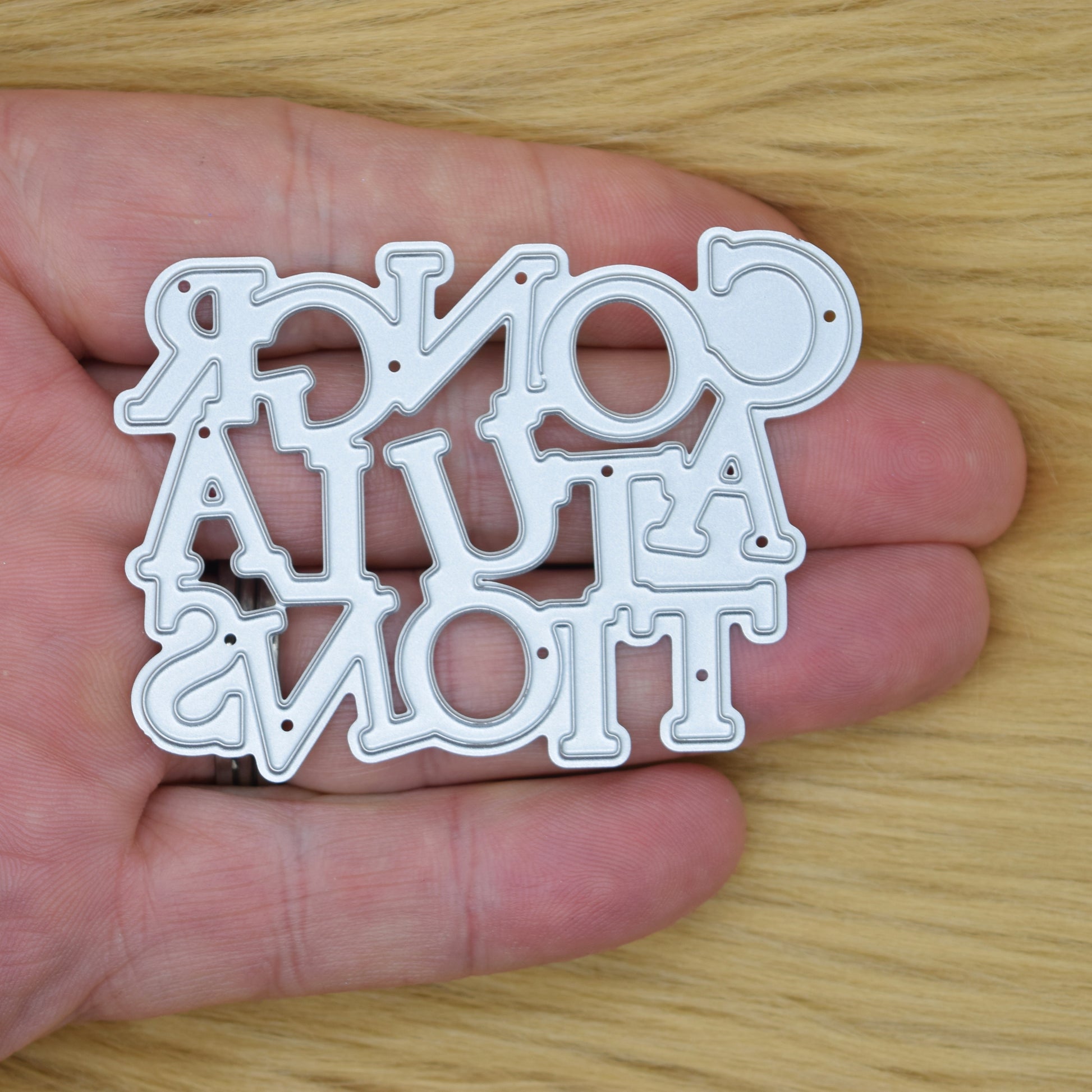 Congratulations sentiment metal cutting die held in hand showing size
