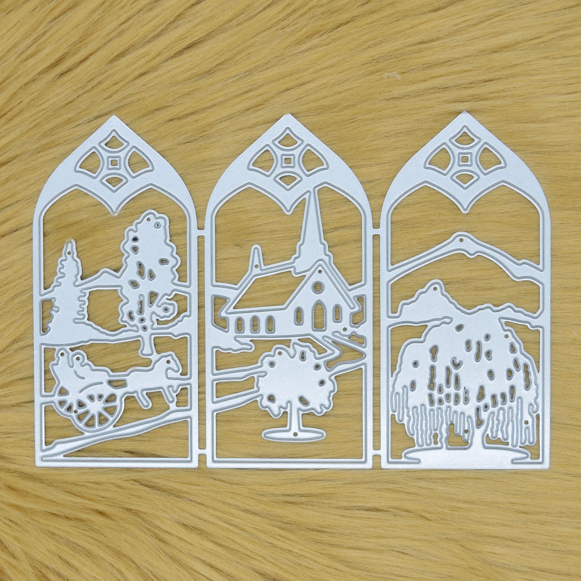 Countryside window scene metal cutting die displayed on a light faux fur background, featuring three connected decorative landscape panels.