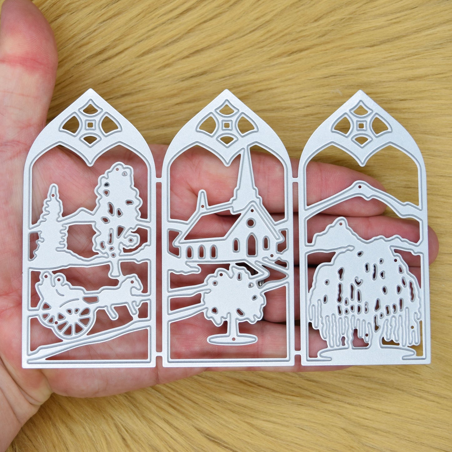 Three-panel countryside window scene metal cutting die shown in hand to demonstrate its size and detailed landscape design.