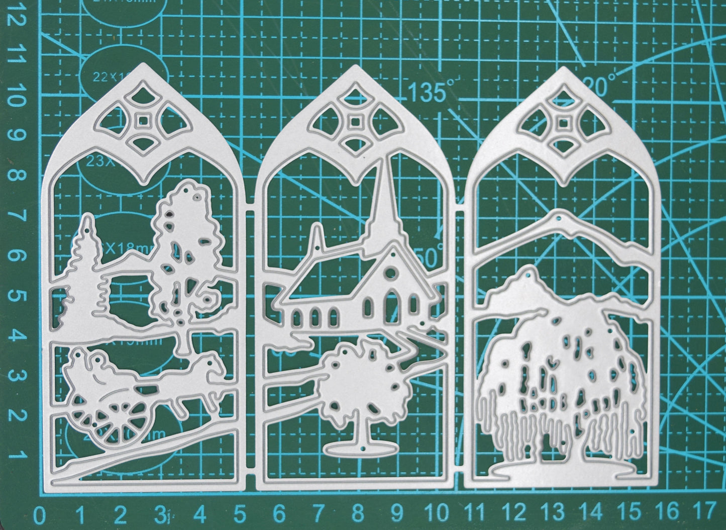 Three-panel countryside window scene metal cutting die displayed on a centimetre cutting mat to demonstrate its overall size.