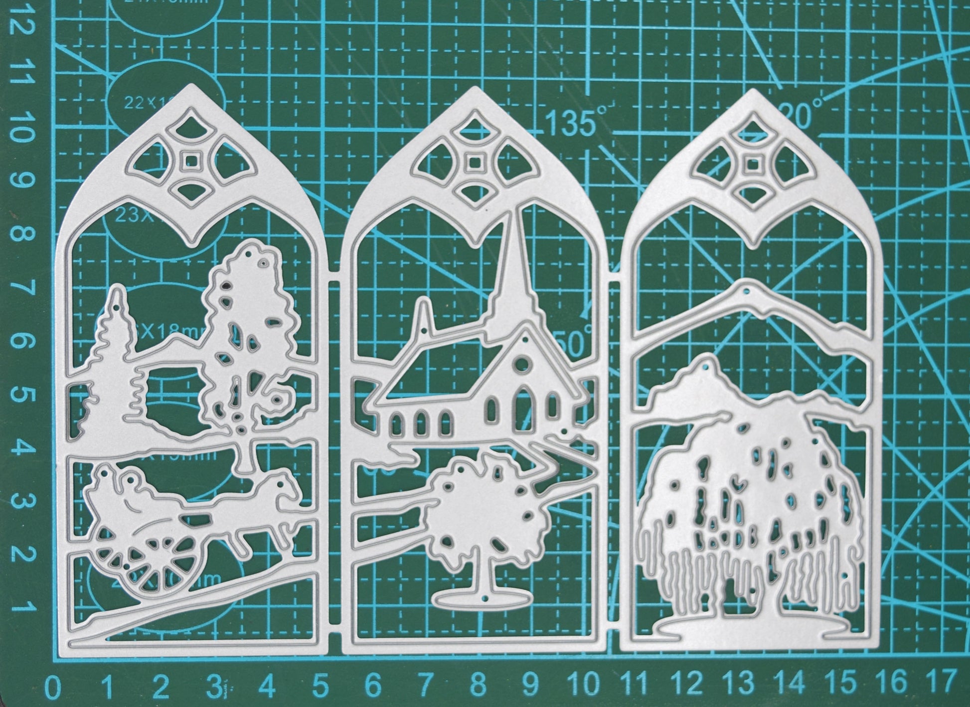 Three-panel countryside window scene metal cutting die displayed on a centimetre cutting mat to demonstrate its overall size.