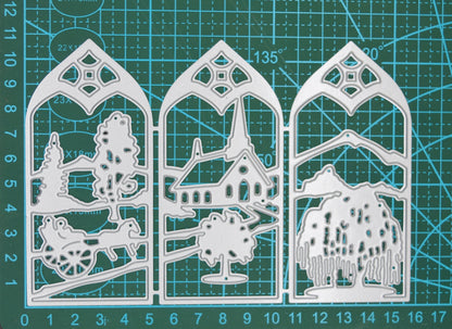Three-panel countryside window scene metal cutting die displayed on a centimetre cutting mat to demonstrate its overall size.