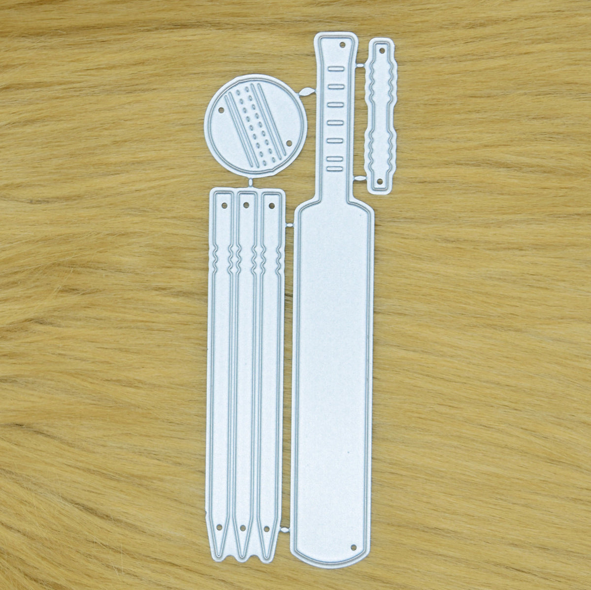 ricket metal cutting die set on a faux fur background featuring a bat, three stumps, ball and bails for card making