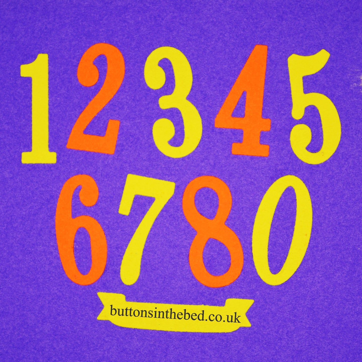 Yellow and orange decorative number die cuts from zero to nine with a banner shape arranged on a purple background.