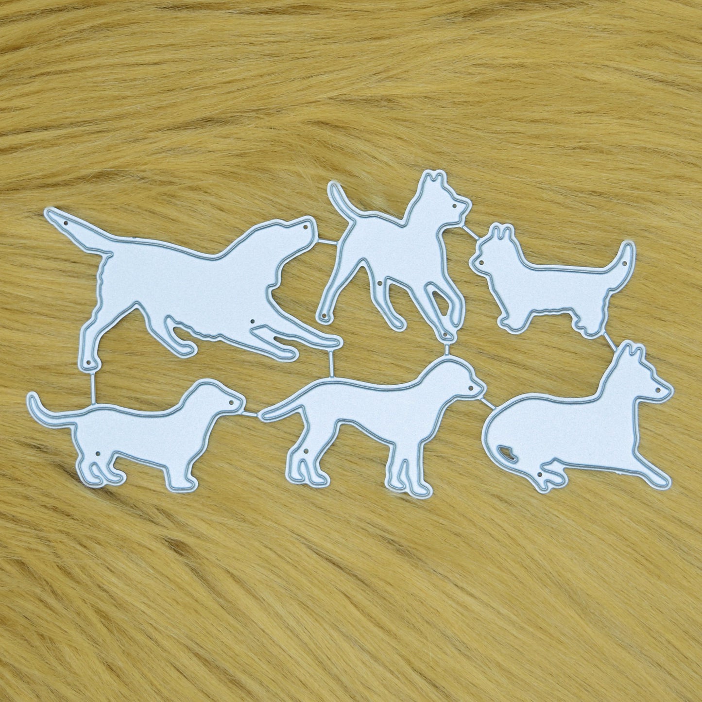 Dog silhouette metal cutting dies set with six pet breed designs displayed on a soft faux fur background for card making and papercraft.