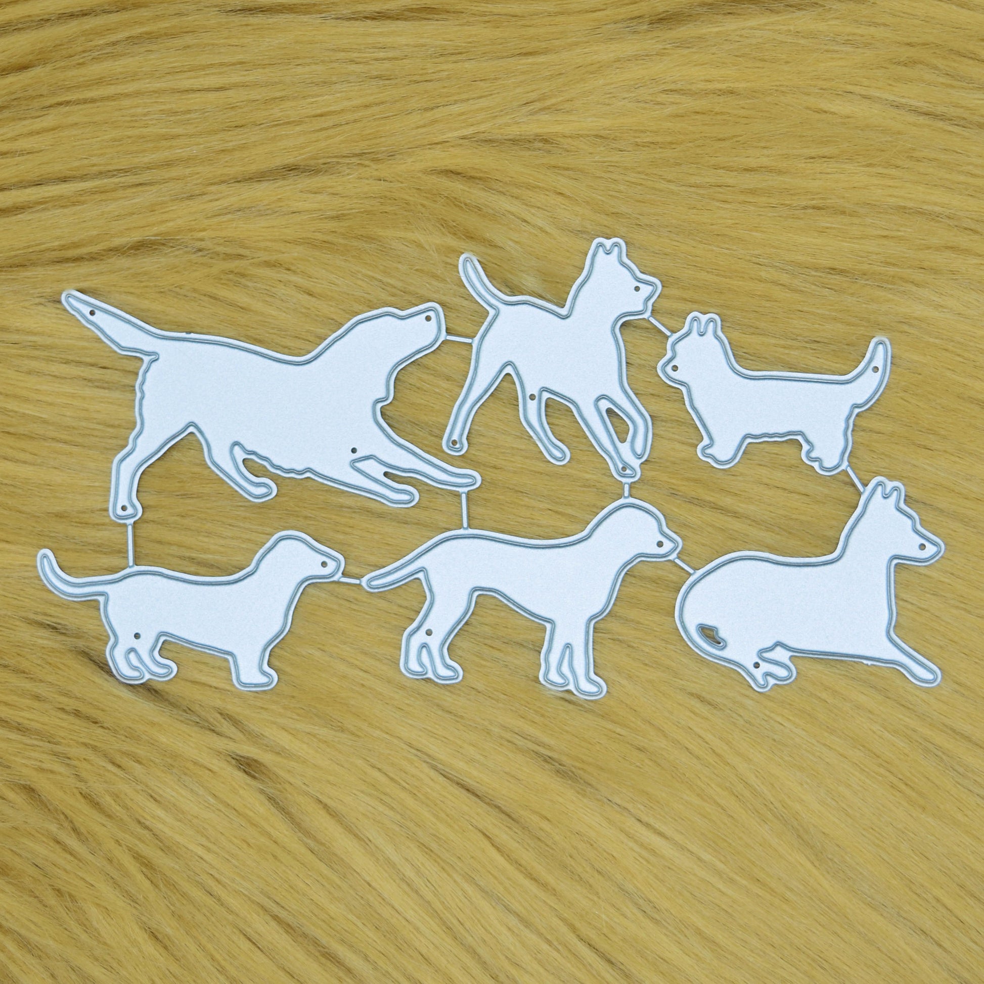 Dog silhouette metal cutting dies set with six pet breed designs displayed on a soft faux fur background for card making and papercraft.