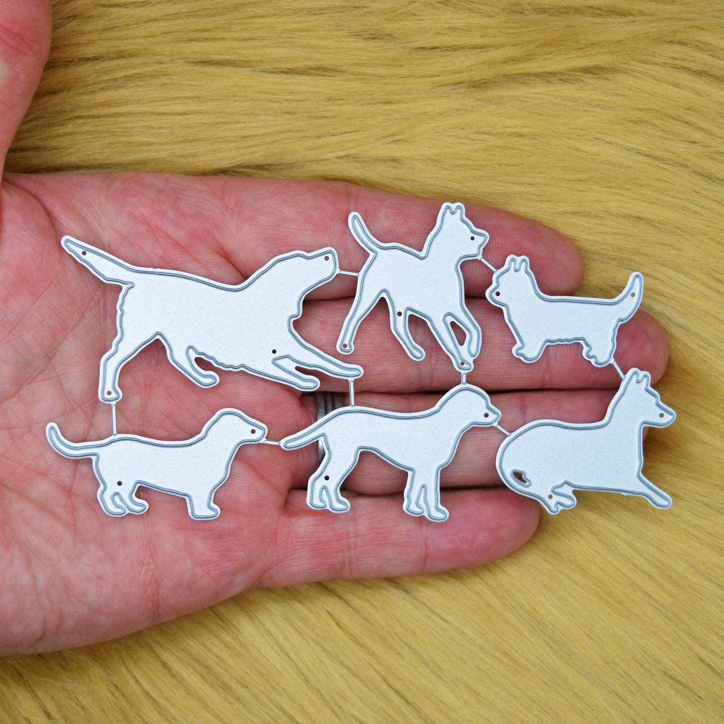 Dog silhouette metal cutting dies set shown in the hand on a soft faux fur background to demonstrate the size of the six pet breed designs.