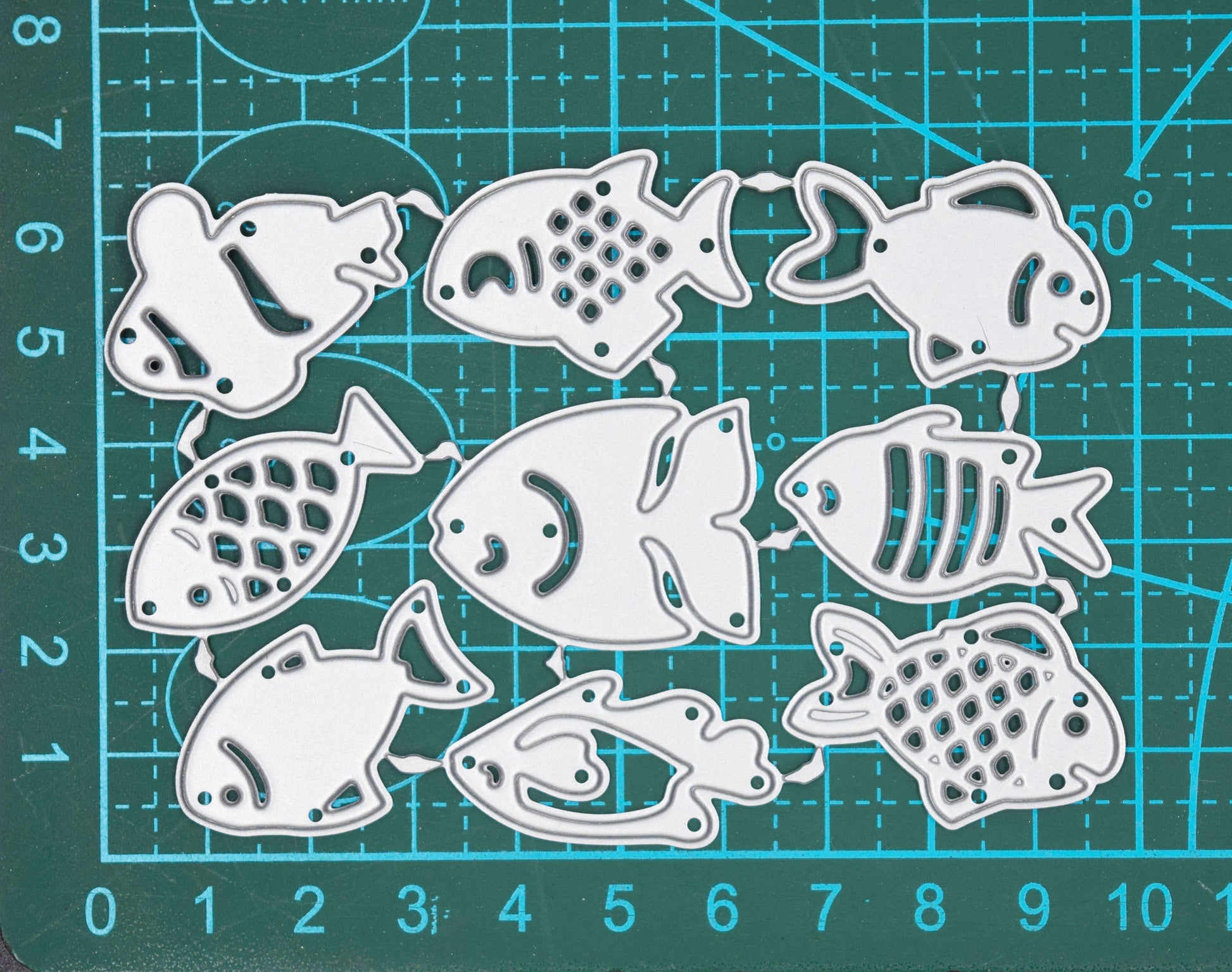 Set of fish metal cutting dies on cutting mat showing size reference