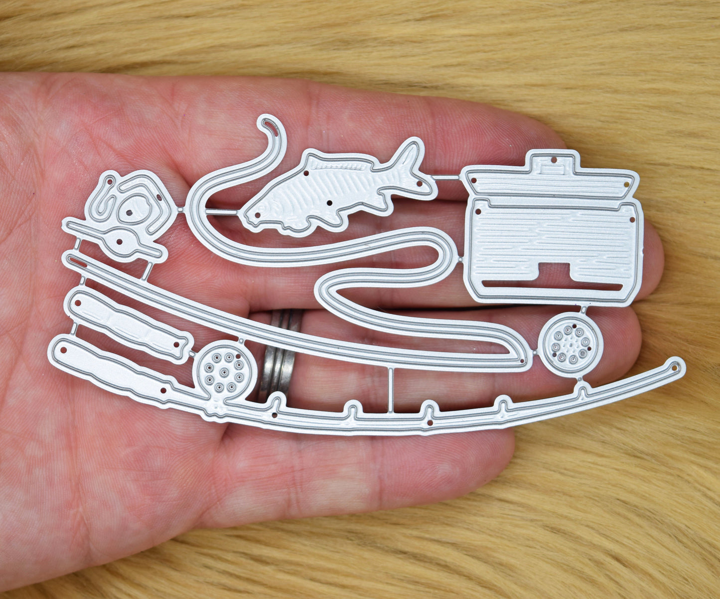 Fishing themed metal cutting dies shown in hand for size reference