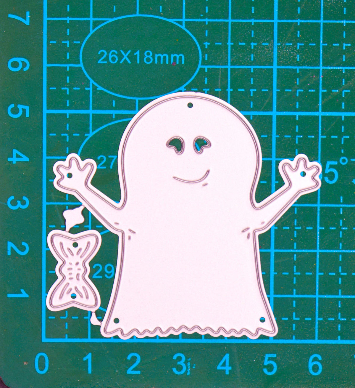Friendly ghost and bow metal cutting die set shown on a centimetre cutting mat for size reference.