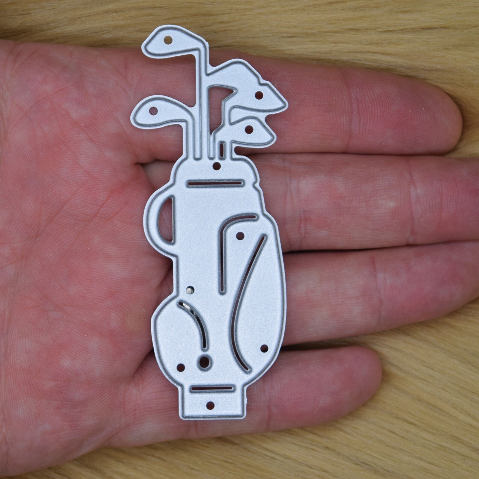 Golf bag metal cutting die held in hand for size showing detailed golf clubs design