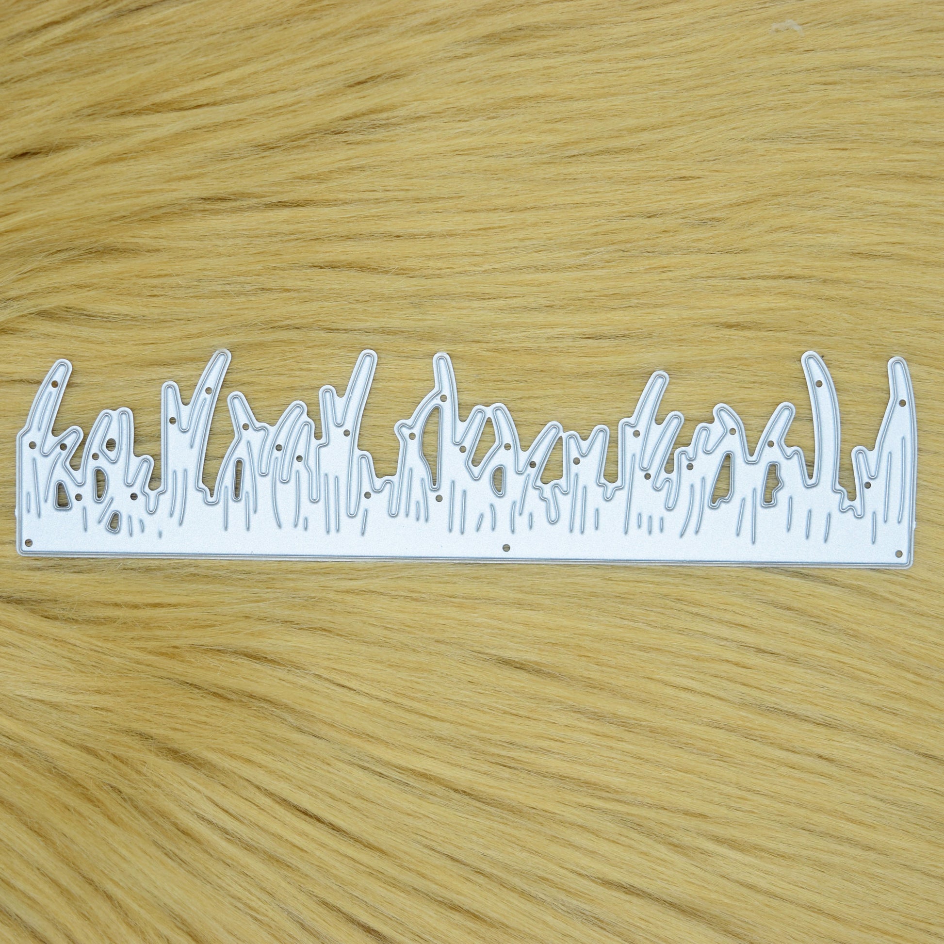 Grass border metal cutting die displayed on a light tan faux fur background for card making and papercraft