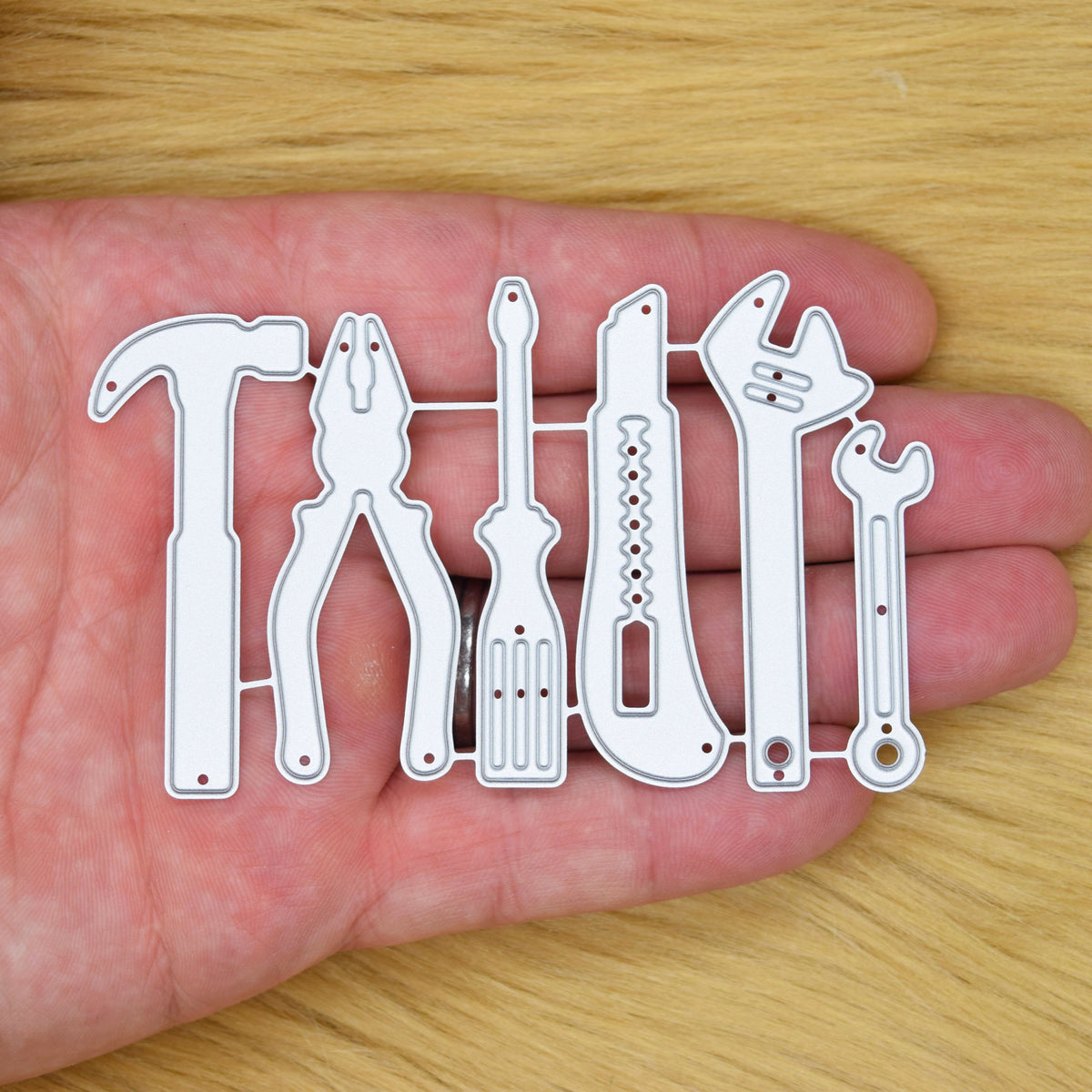 Hand tools metal cutting die set held in hand showing the size of the hammer, pliers, screwdriver, knife and spanner designs.