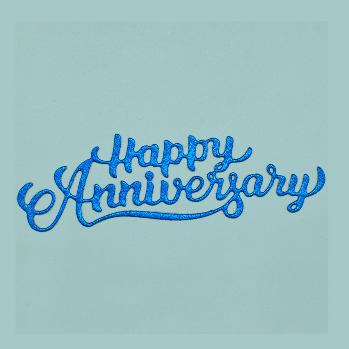 Blue glitter Happy Anniversary script die cut showing the flowing underline and decorative handwritten lettering.