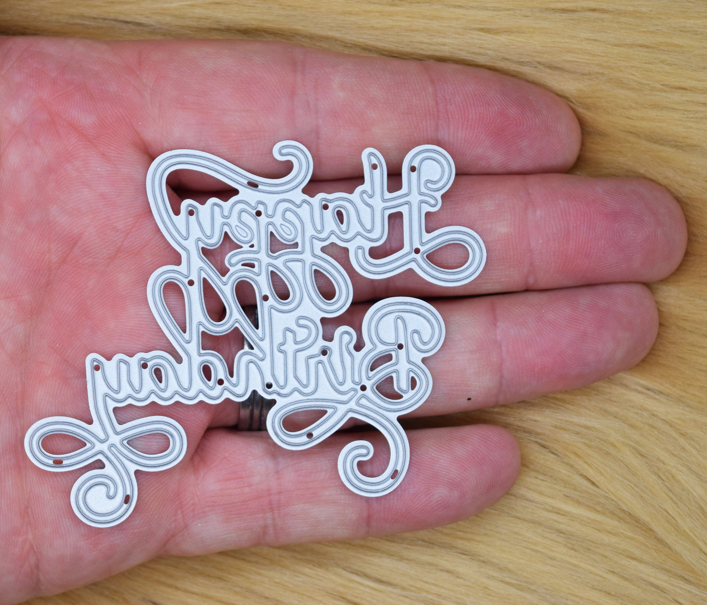 Happy Birthday calligraphy script metal cutting die shown in hand for size reference with decorative swirl sentiment design for card making