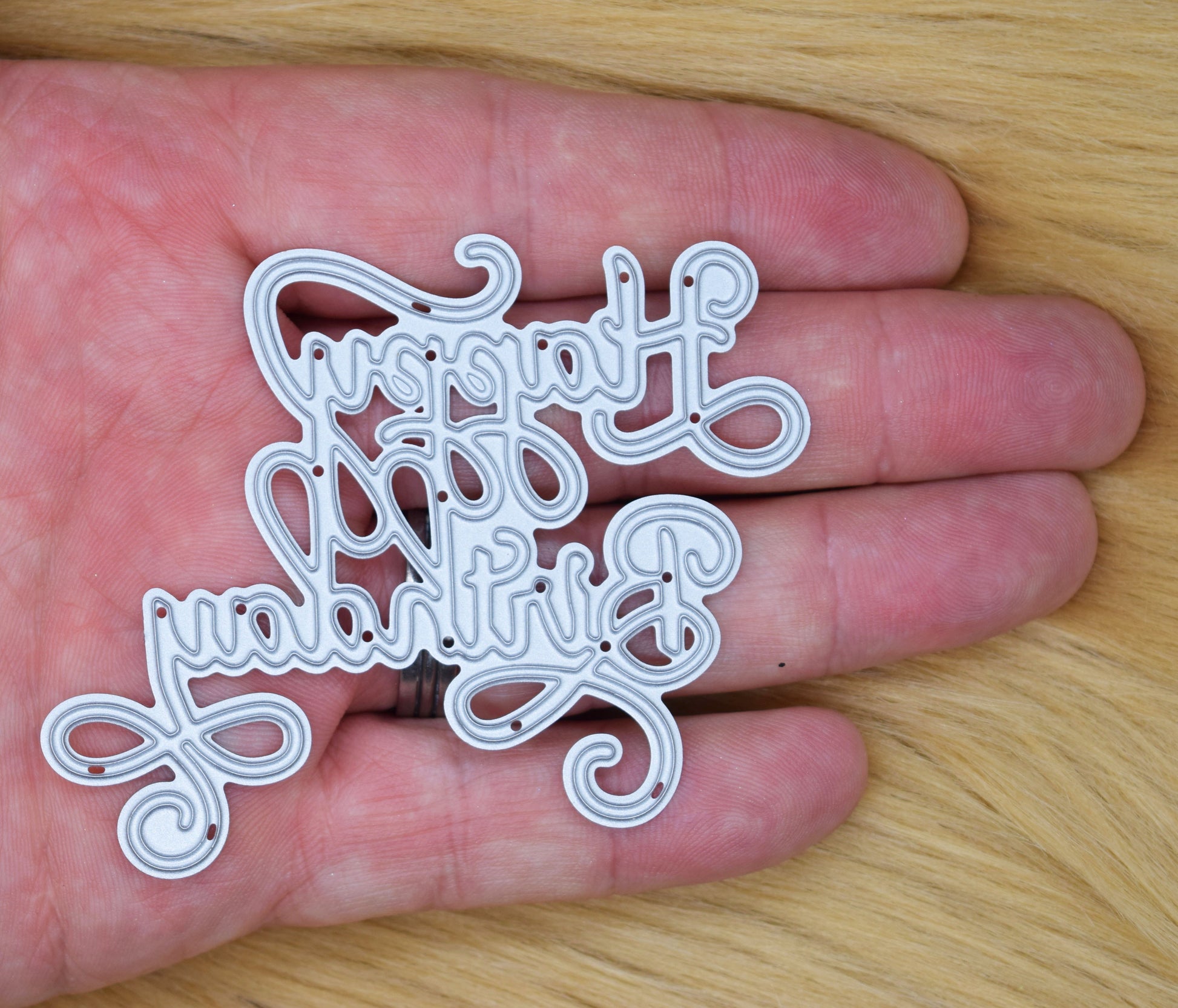 Happy Birthday calligraphy script metal cutting die shown in hand for size reference with decorative swirl sentiment design for card making