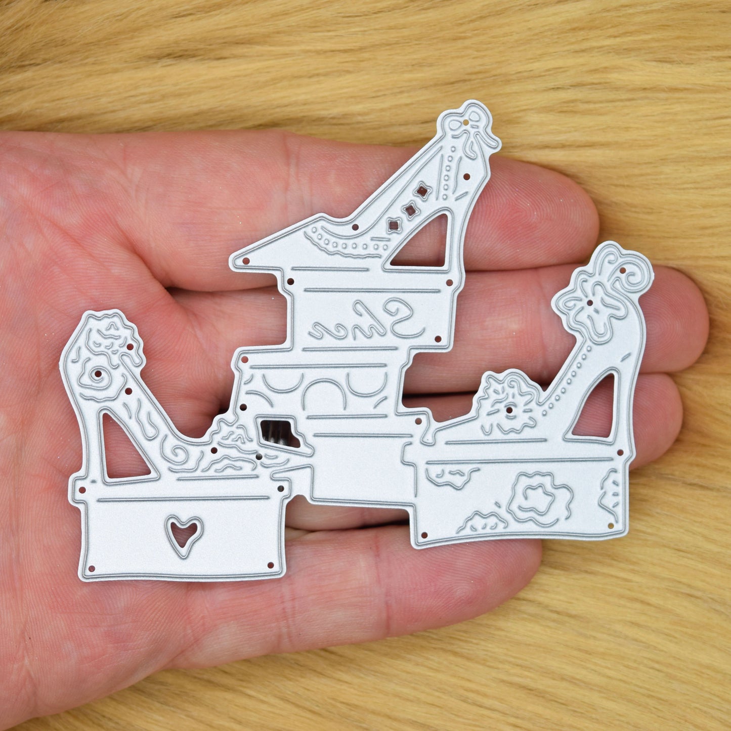 High heel shoes and shoebox metal cutting die held in hand showing approximate size and detail