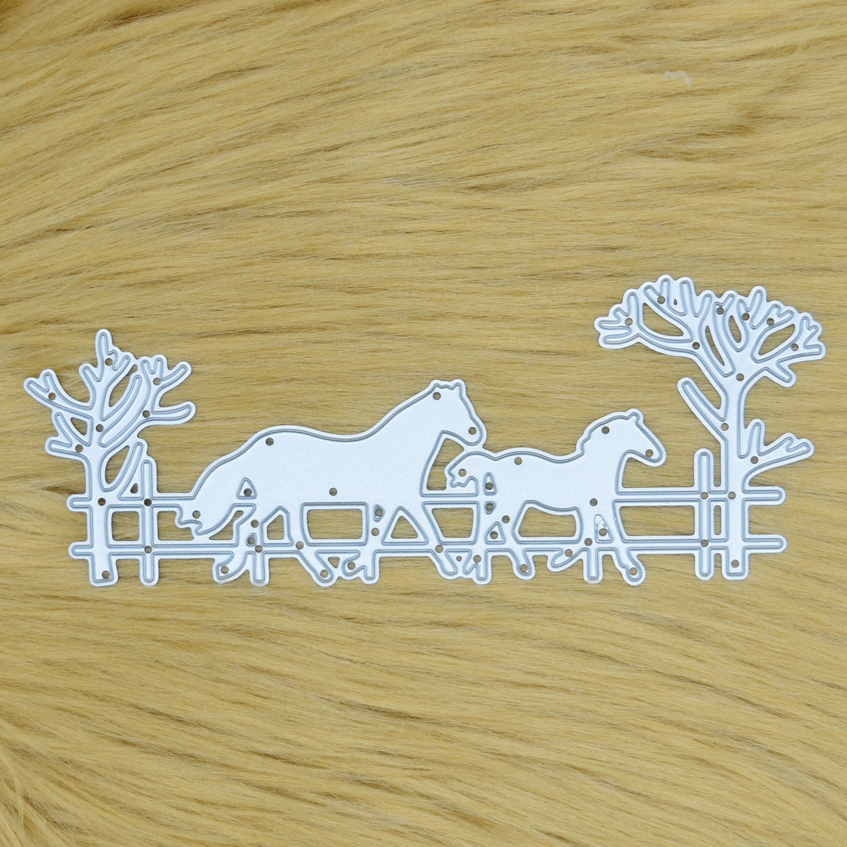 Horse and foal countryside scene metal cutting die with fence and bare trees displayed on a tan faux fur background.