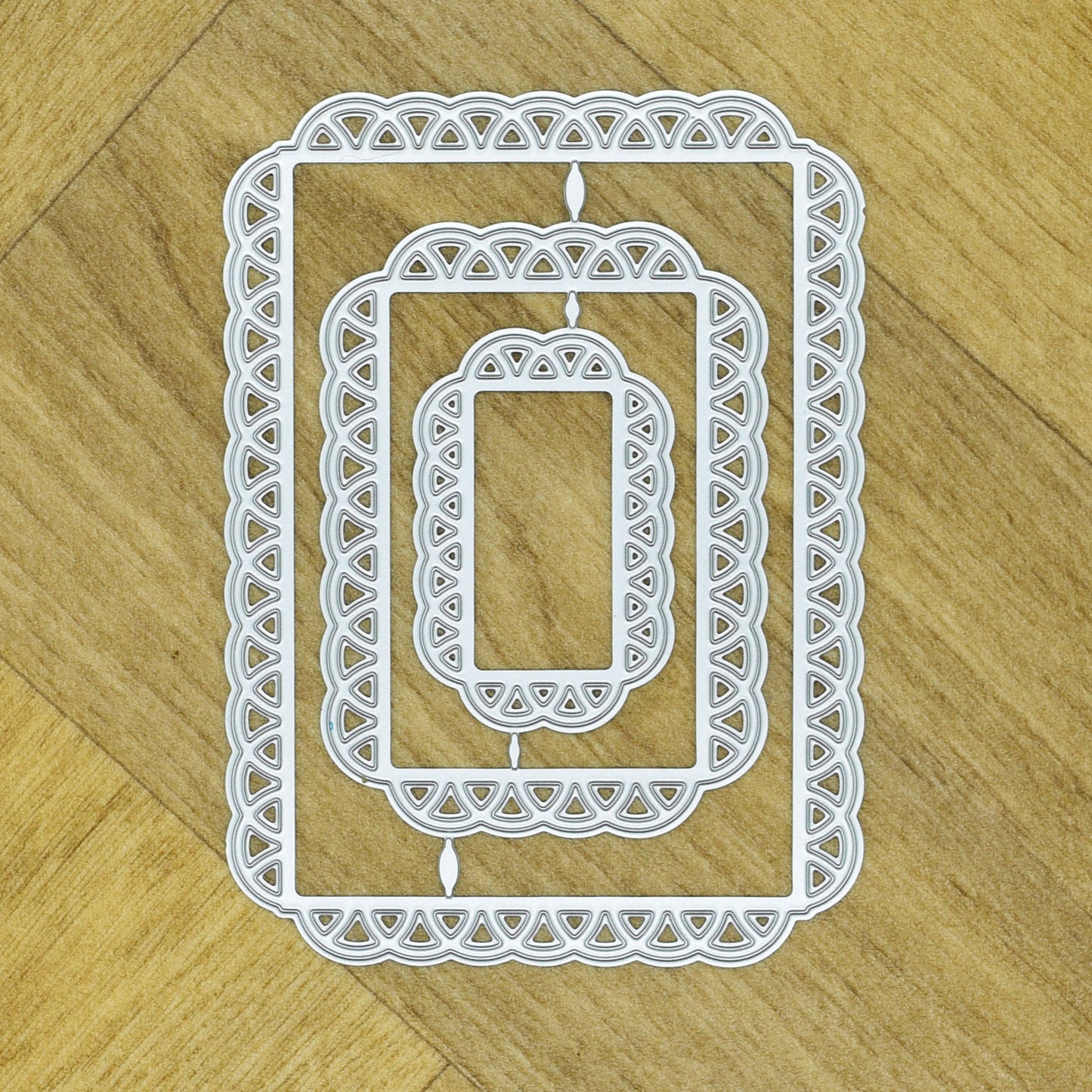 Three graduated lace edge rectangle metal cutting dies nested together on a wood-effect background.