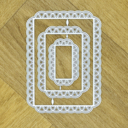 Three graduated lace edge rectangle metal cutting dies nested together on a wood-effect background.