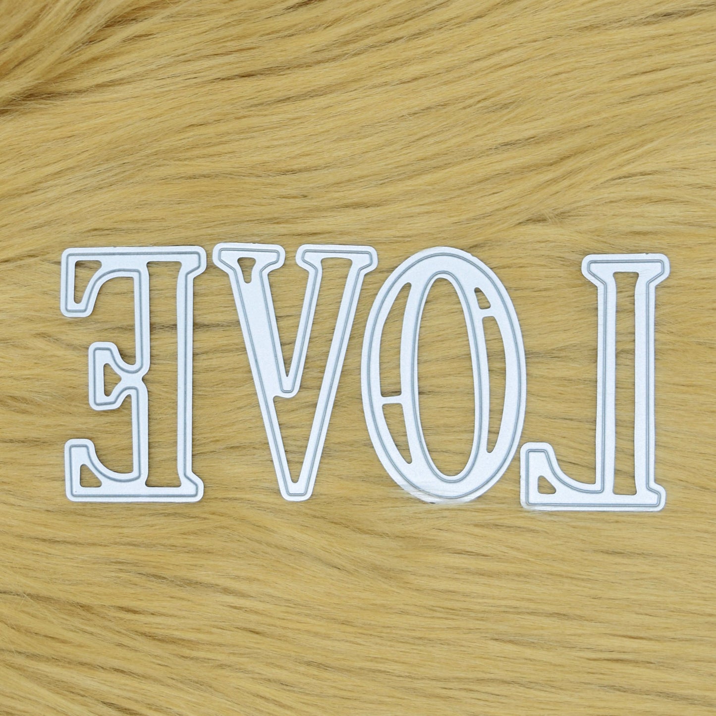 Large uppercase alphabet metal cutting dies arranged to spell LOVE on a faux fur background