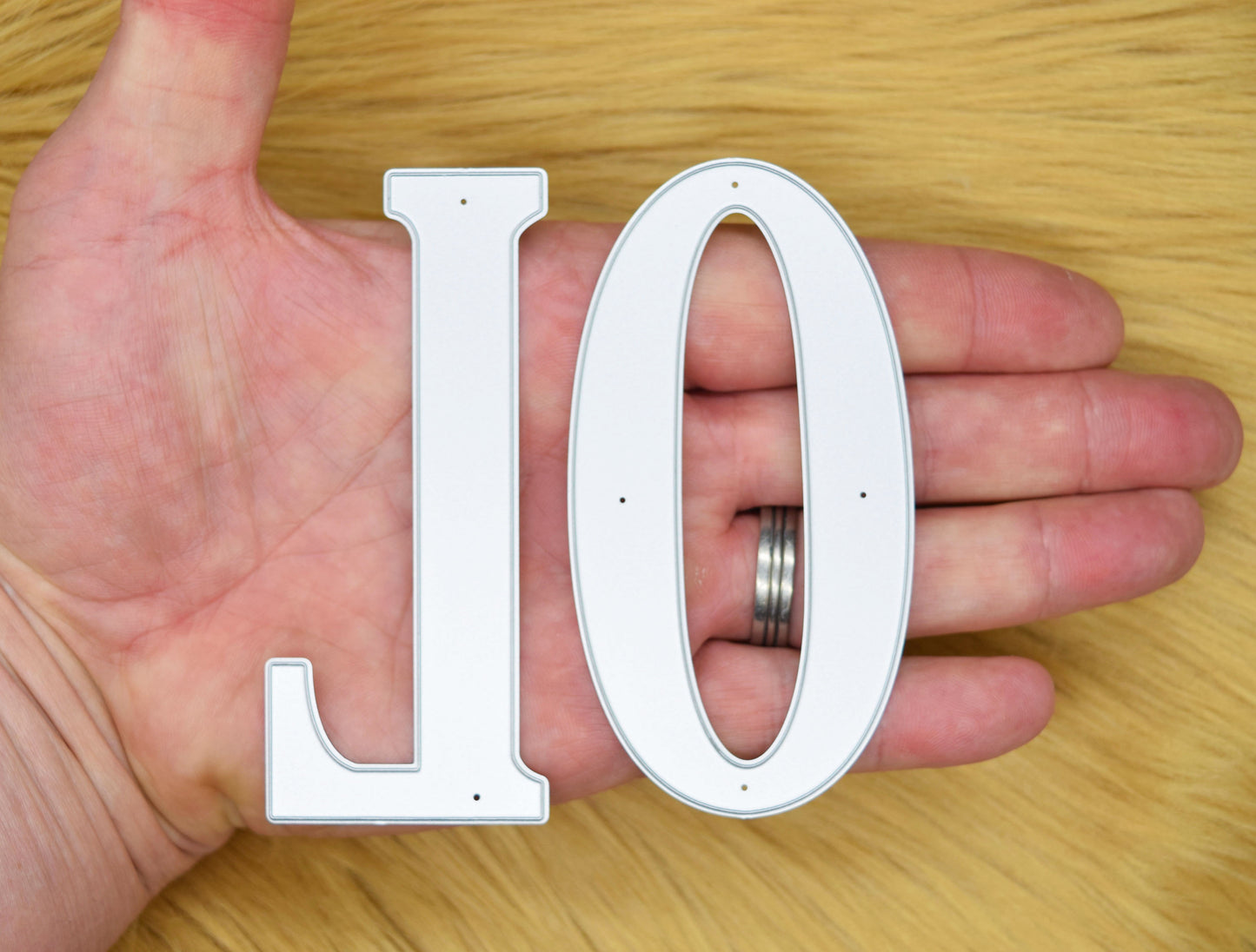 Individual uppercase L and O metal cutting dies held in a hand to show the large serif letter design and scale.